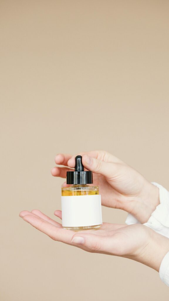 Close-up of hands holding a glass dropper bottle for skincare on beige background.